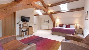 A spacious attic bedroom with exposed wooden beams, a large bed, a desk with a TV, and a cozy seating area. - Cold Cotes Guest House (Harrogate)