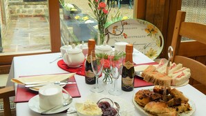A table set with a white tablecloth, two teapots, a vase with flowers, two bottles of champagne, a plate of sandwiches, a bowl of dessert, and a cup of coffee. - Cold Cotes Guest House (Harrogate)
