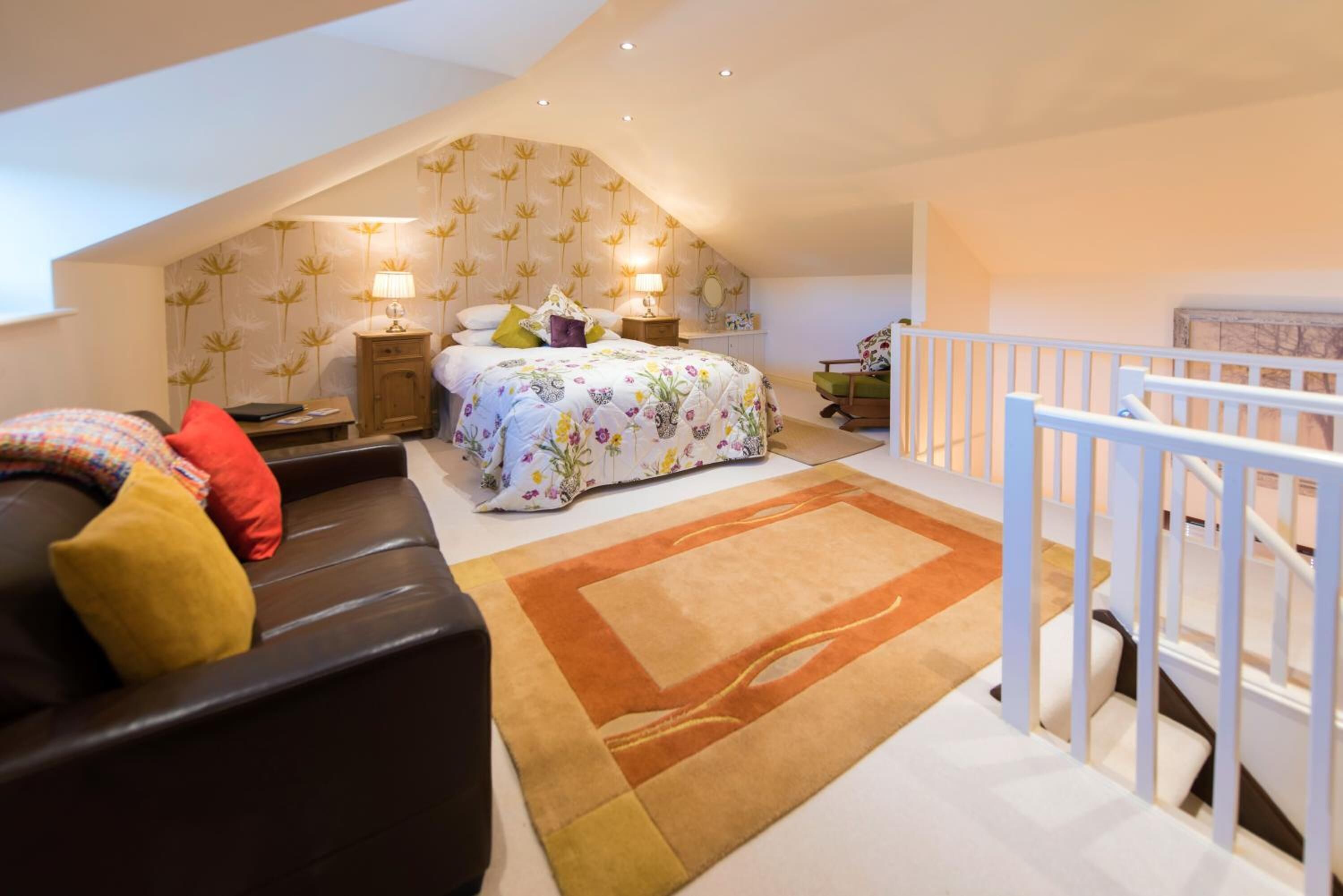 A bedroom with a sloped ceiling, a bed with floral bedding, a nightstand, a lamp, and a view of the outside.