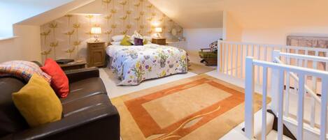 A bedroom with a sloped ceiling, a bed with floral bedding, a nightstand, a lamp, and a view of the outside.