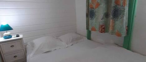 A bedroom with a bed, a nightstand, a lamp, and an air conditioning unit.