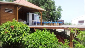 A wooden cabin with a red roof, a covered deck, and a small attached structure.