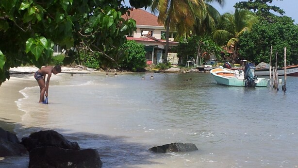 A beach with clear water, a person in a swimsuit, and a boat docked nearby.