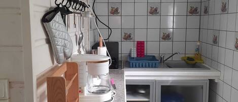A compact kitchen with a coffee maker, a sink, and a small cabinet.