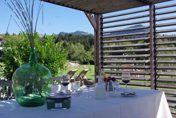 Un espace de restauration en plein air, avec une table dressée pour un repas, entouré de lattes en bois et offrant une vue sur une colline boisée.