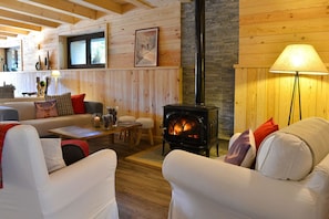 Un salon chaleureux avec un poêle à bois, des canapés blancs et un décor intérieur en bois.