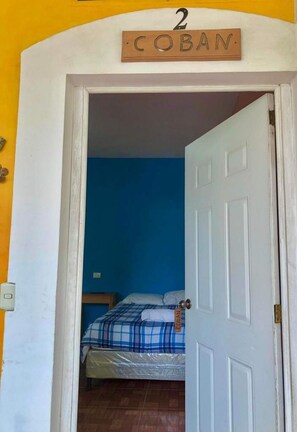 Una habitación con una cama, una pared azul y una puerta con la leyenda 'Coban'.