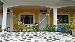 Un patio techado con una hamaca, plantas en macetas y piso de piedra.
