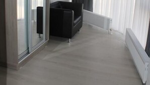 Uma sala de estar moderna com um sofá preto, uma porta de vidro e grandes janelas com cortinas.