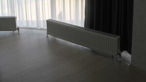 Um quarto com uma janela grande, um radiador e uma cortina escura.