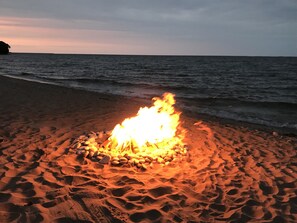 A campfire on a sandy beach with the ocean in the background.