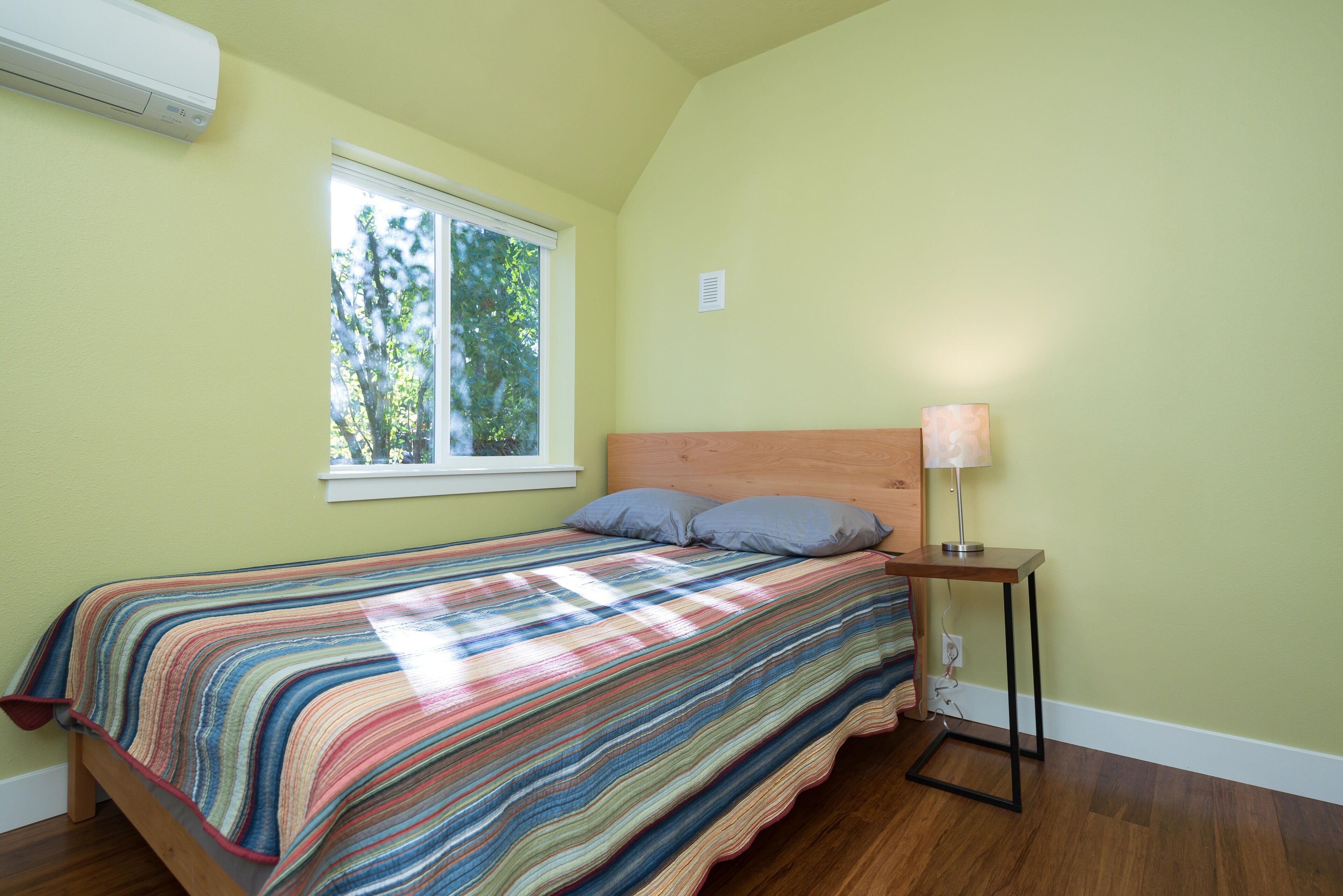 A bedroom with a bed, a window, and a bedside table with a lamp.