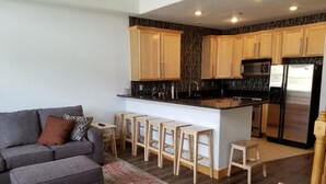 Una cocina moderna con armarios de madera, un refrigerador de acero inoxidable y una zona de bar con taburetes.