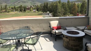 Un patio con mesa y sillas, un pozo de fuego y vistas a un campo de béisbol y montañas.