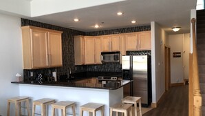 Una cocina moderna con armarios de madera, encimera negra, electrodomésticos de acero inoxidable y una isla central con taburetes de bar.