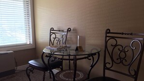 A corner room with a glass table and four chairs, a window with blinds, and a radiator. - Cute cozy condo near ski resorts (Park City)