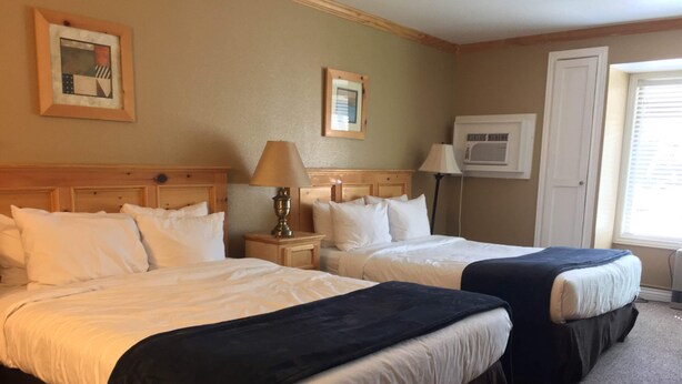 A hotel room with two beds, a nightstand with a lamp, a wall-mounted air conditioner, and a window with blinds. - Cute cozy condo near ski resorts (Park City)