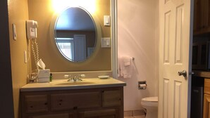 A bathroom with a sink, mirror, toilet, and a door leading to another room. - Cute cozy condo near ski resorts (Park City)