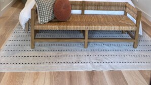 Une chambre avec un banc en bois, un lit recouvert de plusieurs coussins, deux lampes fixées au mur et un ventilateur de plafond.