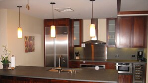 A modern kitchen with a central island, stainless steel appliances, wooden cabinets, and pendant lighting.