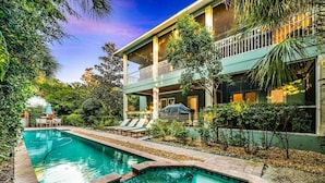 A two-story building with a swimming pool, outdoor seating, and lush greenery.