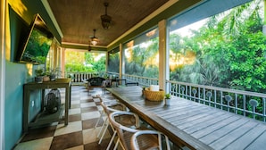 A covered outdoor seating area with a checkered floor, wooden tables, and chairs, overlooking a lush garden.