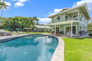 Une maison à deux étages avec une piscine, du mobilier d’extérieur et une pelouse bien entretenue.
