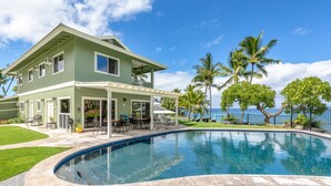 Une maison à deux étages avec une piscine, du mobilier d’extérieur et des palmiers.
