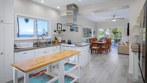 Une cuisine moderne avec des meubles blancs, une table à manger en bois et une vue sur l’océan.