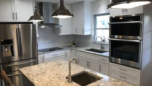 Una cocina moderna con electrodomésticos de acero inoxidable, encimeras de granito e iluminación colgante.