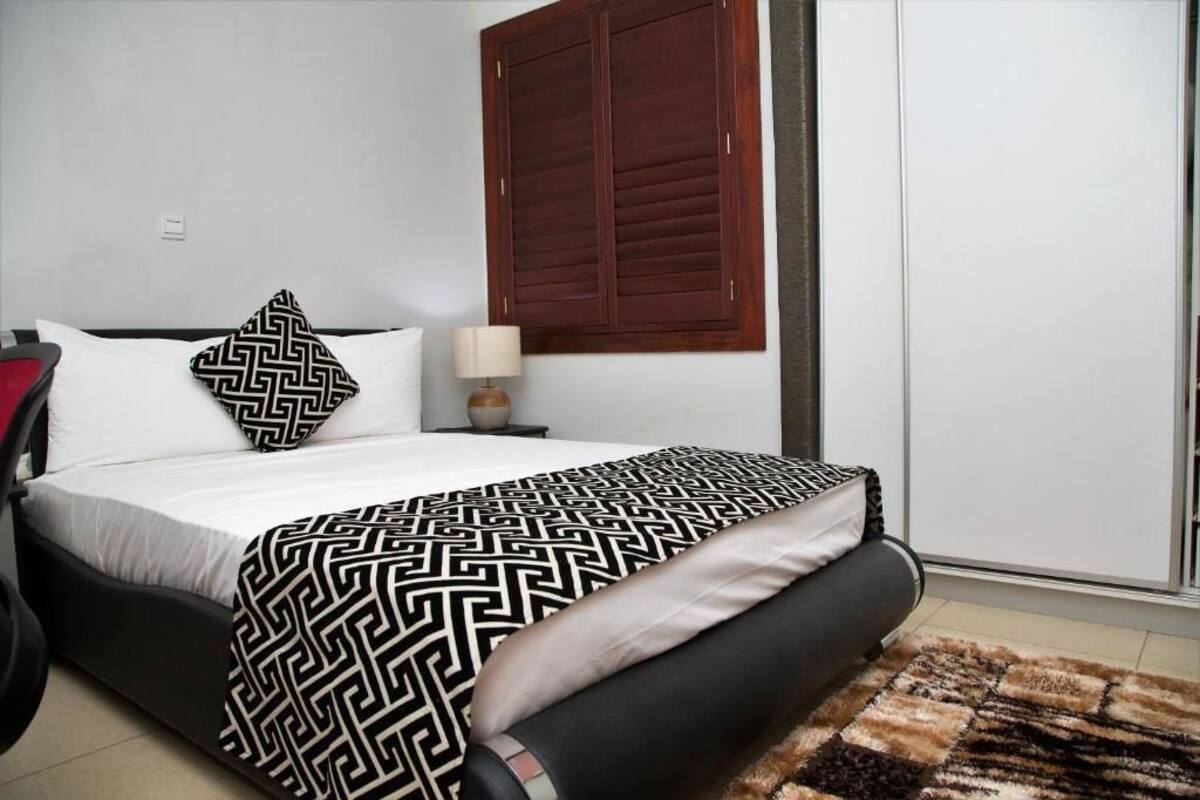 A bed with a patterned bedspread, a bedside lamp, and a window with wooden shutters.