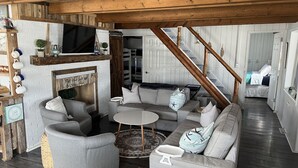 Una sala de estar acogedora con chimenea, vigas de madera y una escalera que lleva a un dormitorio.
