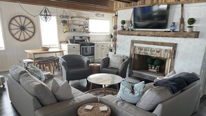 Un salón acogedor con un sofá gris, un reposapiés de mimbre y una chimenea con un letrero que dice 'Pon los pies en alto'.