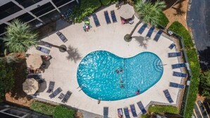 An aerial view of a swimming pool surrounded by lounge chairs and palm trees, with a building in the background. - Sandy Feet Retreat-New Shower-Bikes Incl-Oceanview (Hilton Head Island)