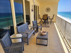 A balcony with a view of the ocean, featuring a seating area with a table and chairs, a small round table with a bowl, and a decorative wall piece. - Gorgeous 2 Bedroom, King Beds; Spectacular Gulf Views; Newly renoated (Panama City Beach)