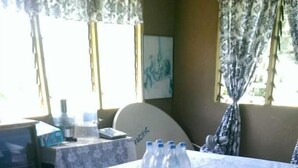 A hotel room with a table set for dining, a patterned carpet, and a window with curtains. - Lady Maria's Place (Pangai)