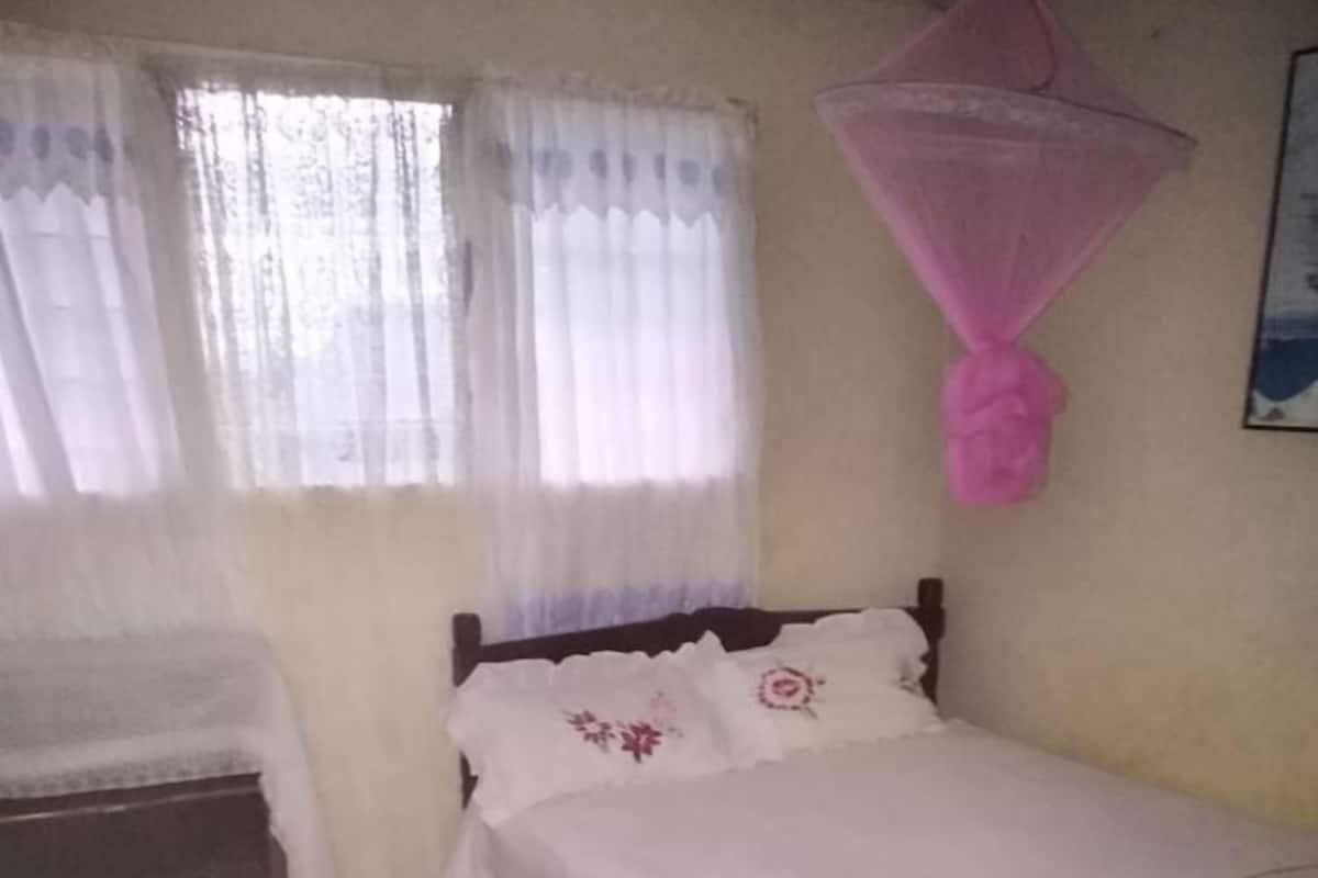Un dormitorio con cama, mesita de noche, piso a cuadros y ventana con cortinas.