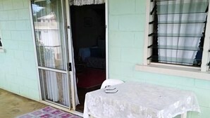 A room with a table covered by a white tablecloth, a patterned rug, and a sliding glass door leading to another room. - Lady Maria's Place (Pangai)