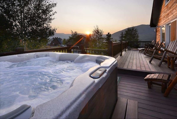 A wooden deck with a hot tub, outdoor seating, and a view of the sunset.