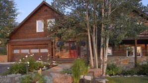 A wooden house with a garage, stone foundation, and a landscaped garden with various plants and a tree. - Ruby Retreat (Crested Butte)