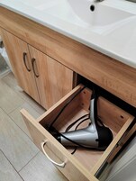 Un baño con lavamanos blanco, muebles de madera y un cajón que contiene un secador de pelo.