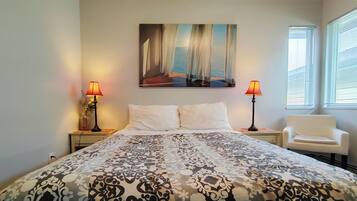 A bedroom with a bed, two bedside lamps, a chair, a painting on the wall, and a window with blinds.