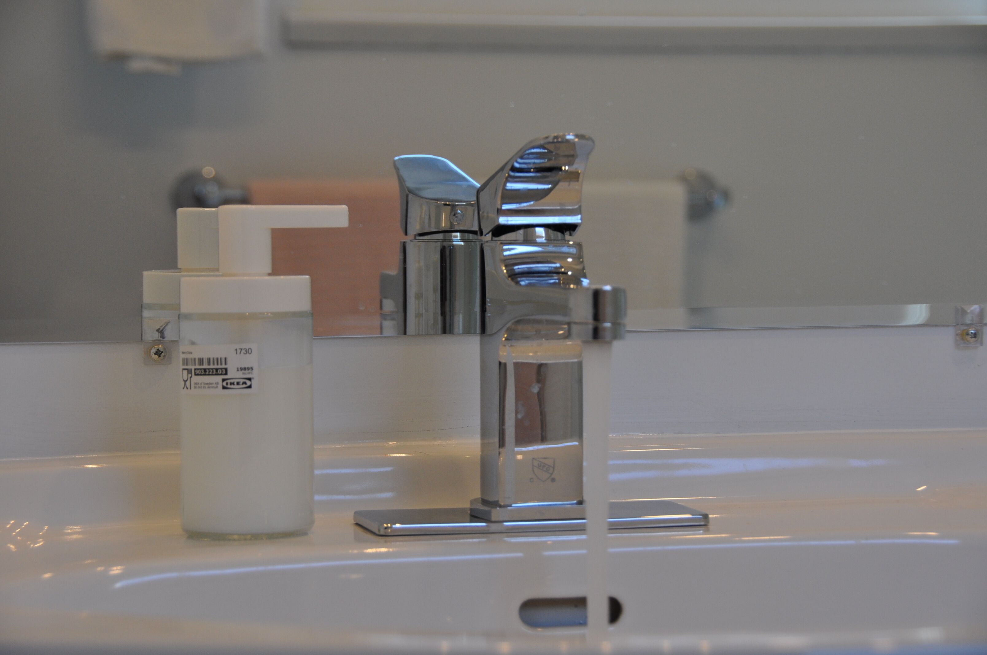 A bathroom sink with a chrome faucet, a soap dispenser, and a mirror above it.