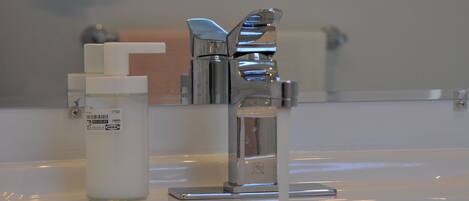 A bathroom sink with a chrome faucet, a soap dispenser, and a mirror above it.