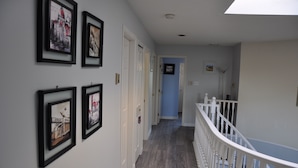 A hallway with framed artwork on the walls, a staircase with white railings, and a blue door at the end. - Better Bed House (Richmond)