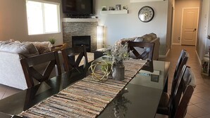 En matplats med ett glasbord, mörka stolar, en öppen spis, en väggmonterad TV och en klocka på väggen.
