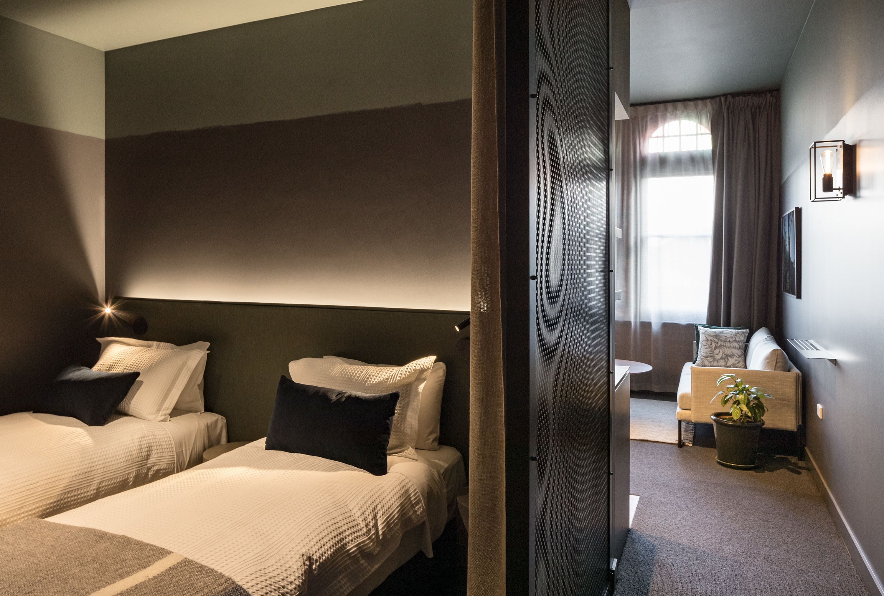A hotel room with two beds, a small table, a sofa, and a potted plant.