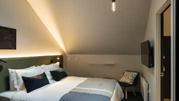 Un dormitorio moderno con tragaluz, una cama con manta a rayas, una silla y un televisor de pantalla plana en la pared.