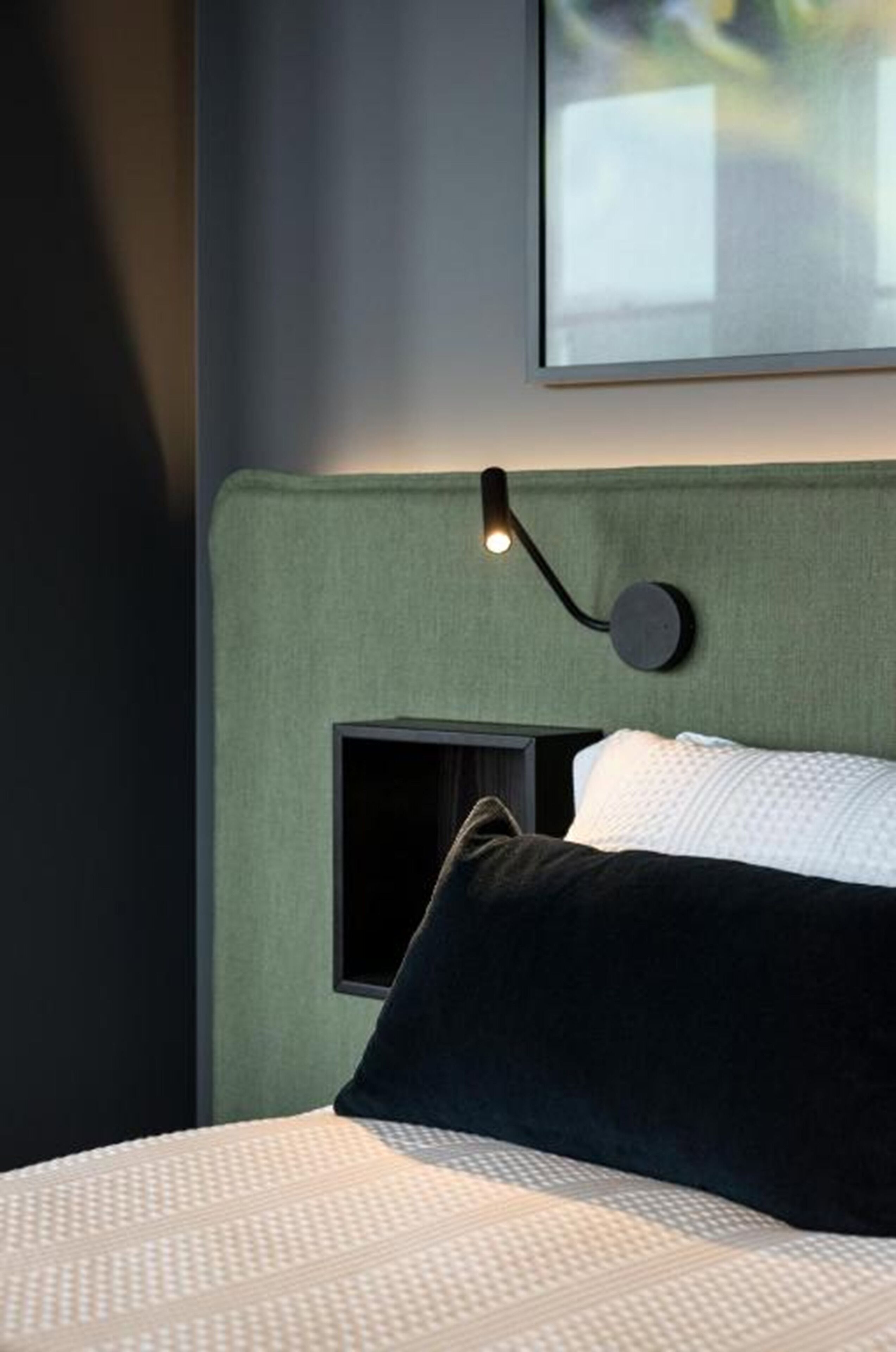 A neatly made bed with a patterned bedspread, a dark pillow, and a headboard with a built-in light fixture.