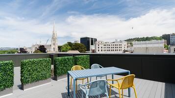 Enjoy a rooftop retreat with a city view, featuring a table and two chairs amidst lush hedges.